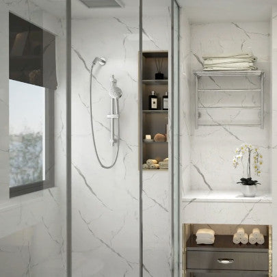 A modern bathroom featuring a sleek handheld shower with a chrome finish, mounted on a marble wall. The space is elegantly designed with a glass partition, minimalistic decor, and natural light streaming through a window.